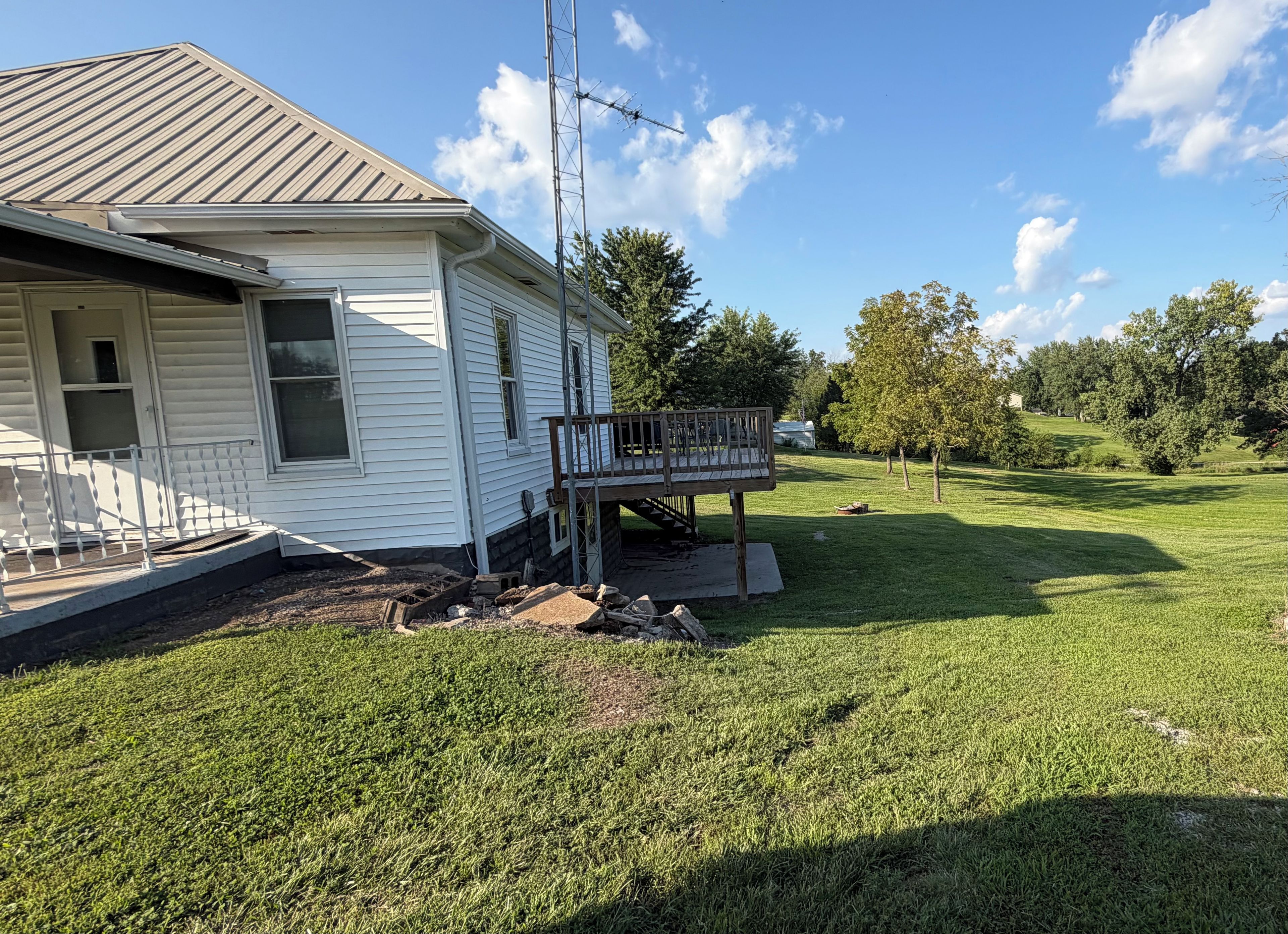 A white house with a metal roof, a wooden deck, and a grassy yard.