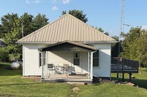 A small white house with a porch, a metal roof, and a satellite dish.
