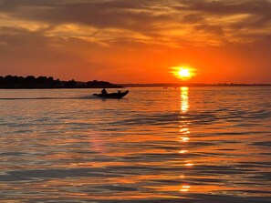A sunset over a calm body of water with a silhouette of a boat and distant shoreline.