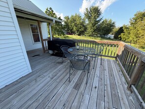 A wooden deck with a barbecue grill and metal chairs.