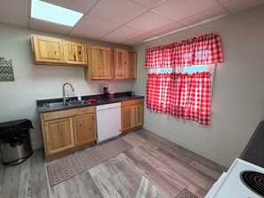 A kitchen with wooden cabinets, a dishwasher, a sink, and a window with red and white checkered curtains.