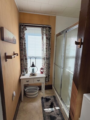 A small bathroom with a wooden vanity, a window with patterned curtains, a radiator, and a door with a wooden handle.