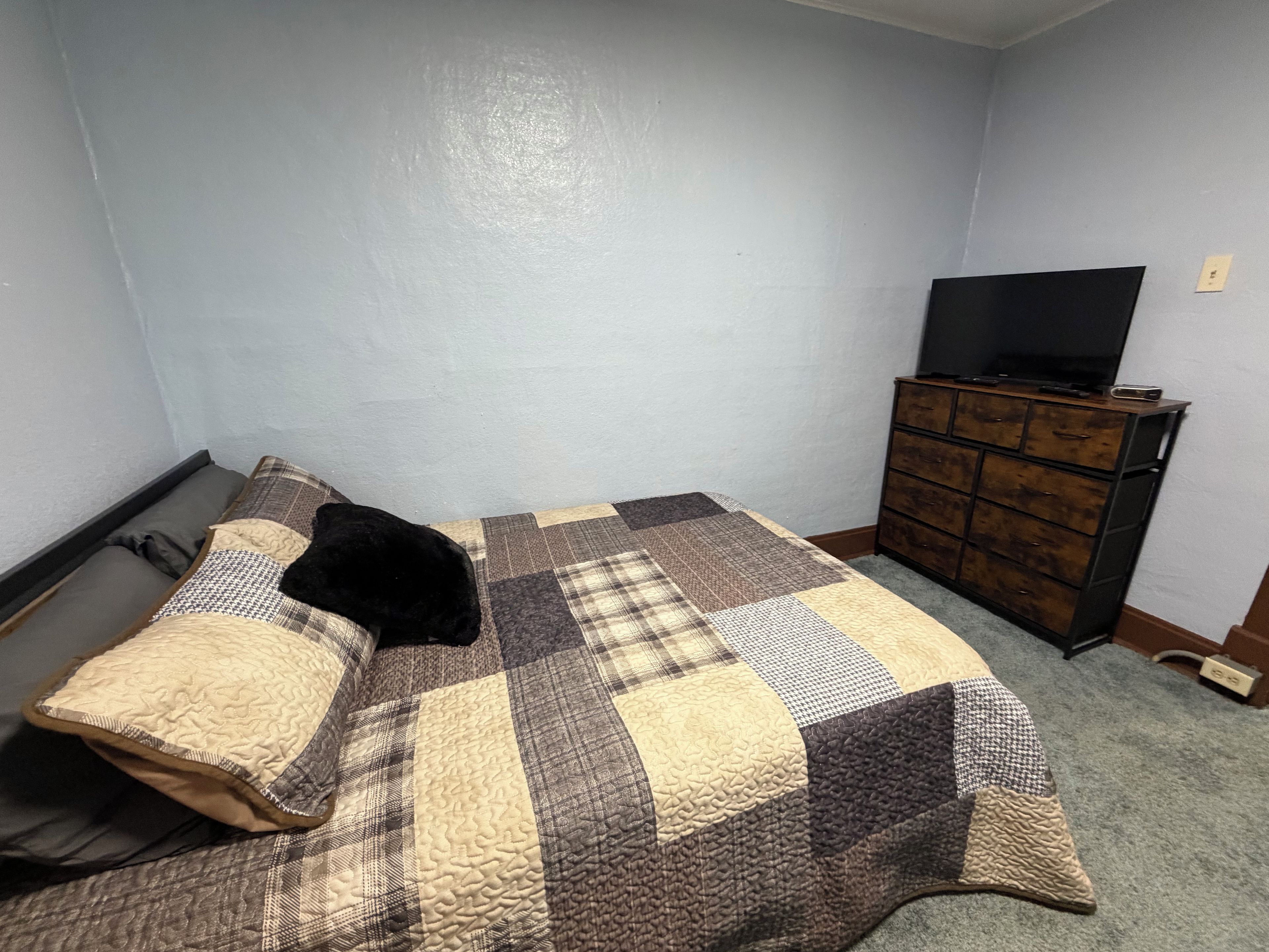 Une chambre à coucher avec un lit, un téléviseur posé sur une commode et un sol recouvert d’une moquette.
