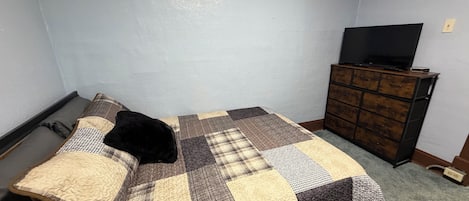 Un dormitorio con cama, televisor en una cómoda y piso alfombrado.