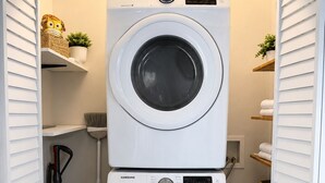 Ein Waschraum mit zwei Samsung-Waschmaschinen, einem Staubsauger und Regalen mit Handtüchern und Körben.