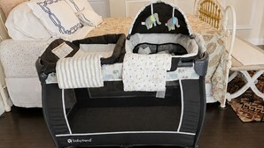 Ein Babybettchen auf Rädern, eine geblumte Bettdecke und ein weißes Kopfteil.