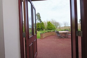 A view through a wooden door into a covered patio area with a brick wall, a table, and chairs. - Chomley @ Summerfield Farm (Whitby)
