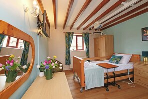 A bedroom with a wooden bed, a bedside table, a mirror, a wardrobe, and a window with curtains. - Chomley @ Summerfield Farm (Whitby)