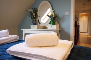 A bedroom with a bed, a bedside table with a mirror, and a vase with flowers. - Chomley @ Summerfield Farm (Whitby)