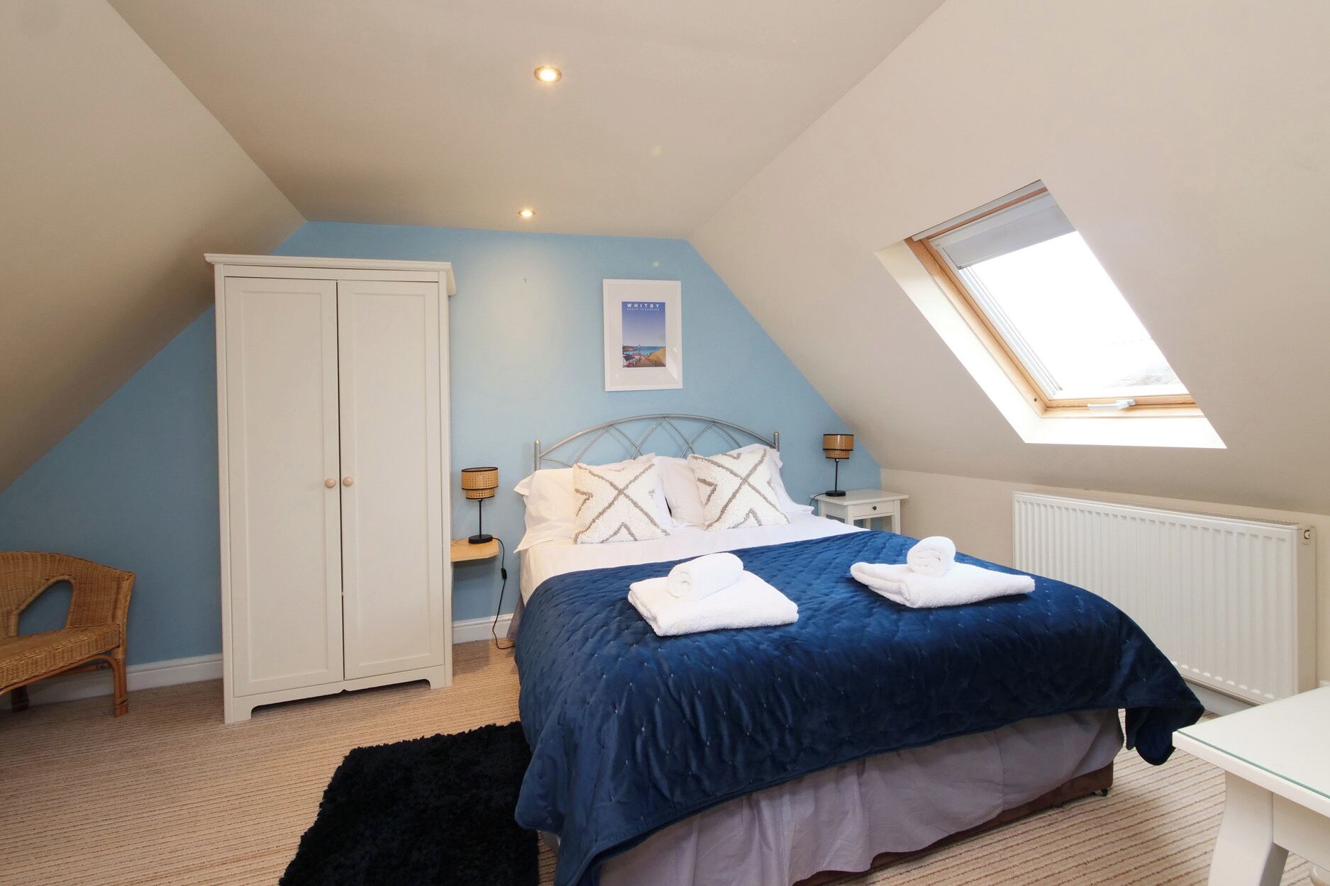 A bedroom with a bed, a wardrobe, a desk, a chair, a window, and a picture on the wall.