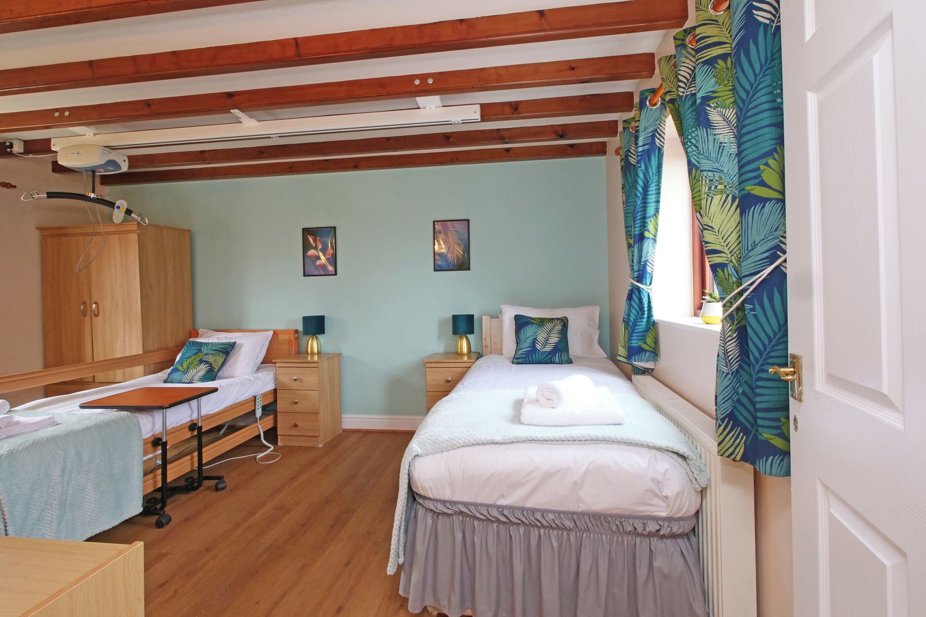 A bedroom with two beds, wooden flooring, a wardrobe, bedside tables with lamps, and a ceiling fan.