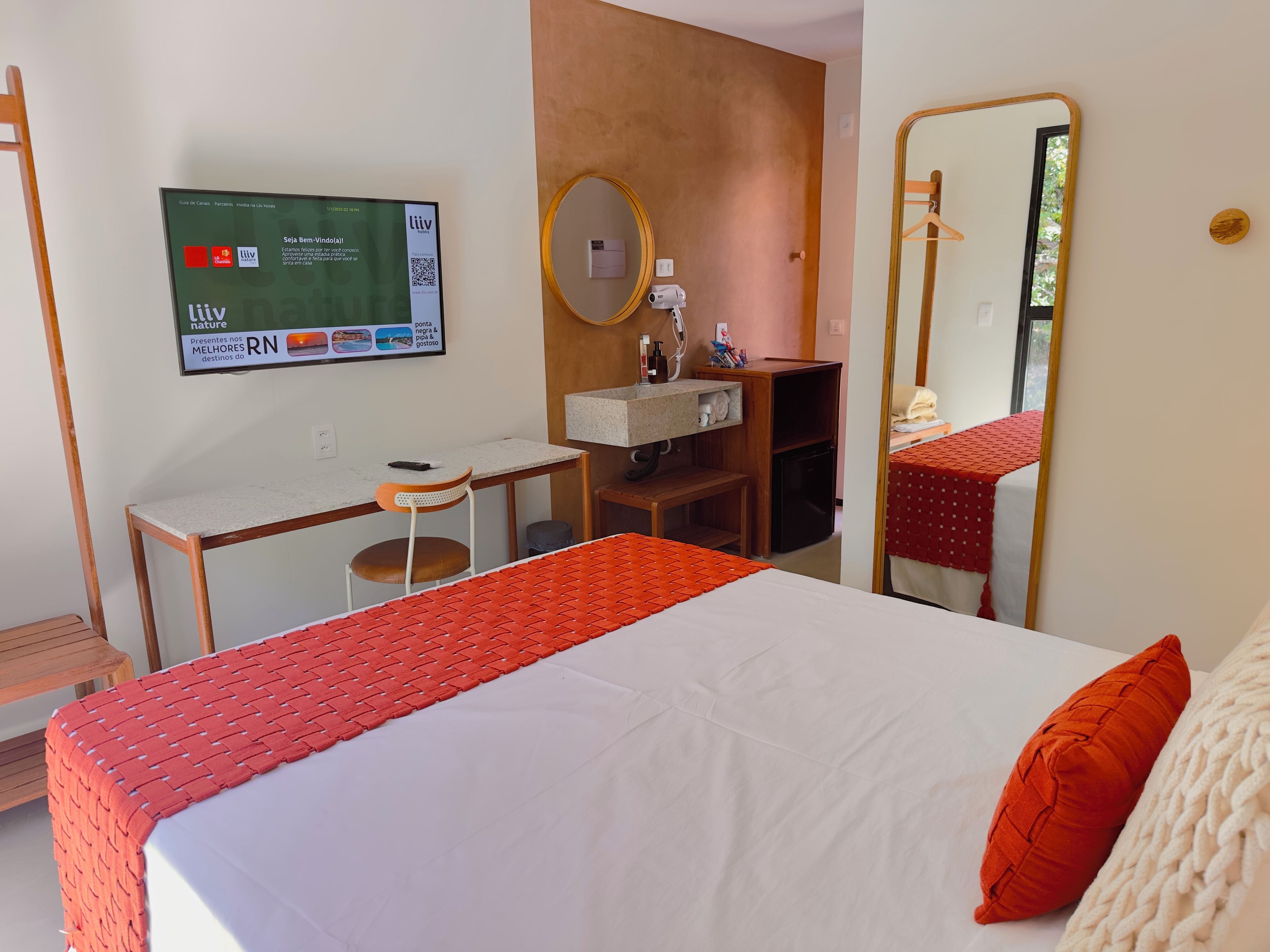 A hotel room with a bed, a desk, a chair, a mirror, and a television displaying a menu.