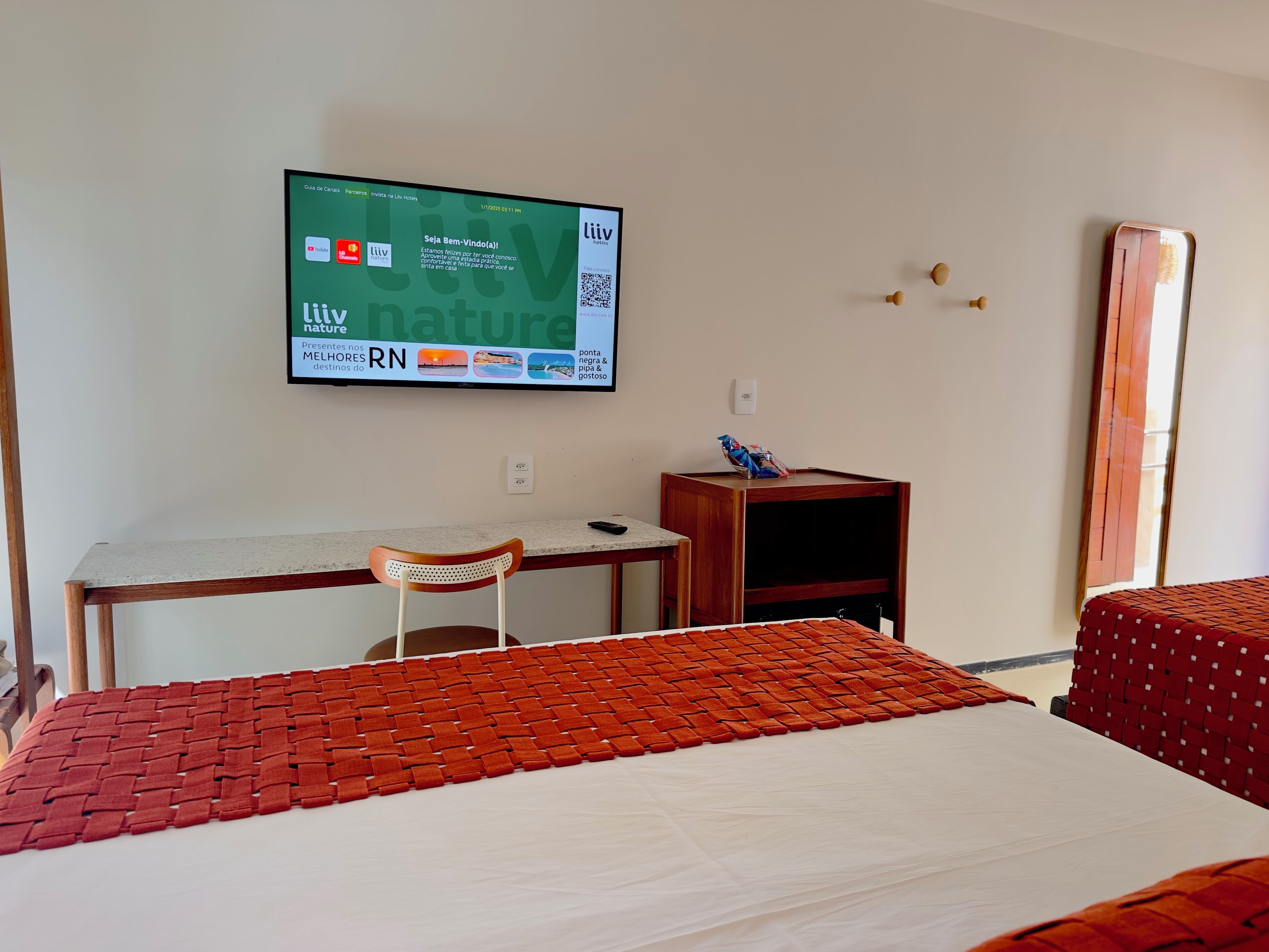 Ein Hotelzimmer mit Bett, Schreibtisch, Stuhl, Wandfernseher und einem kleinen Nachttisch.