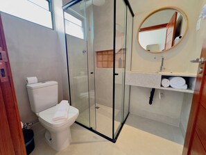 A modern bathroom with a glass-enclosed shower, a toilet, a sink with a mirror, and a towel rack. - Liiv Nature Pipa (Tibau do Sul)