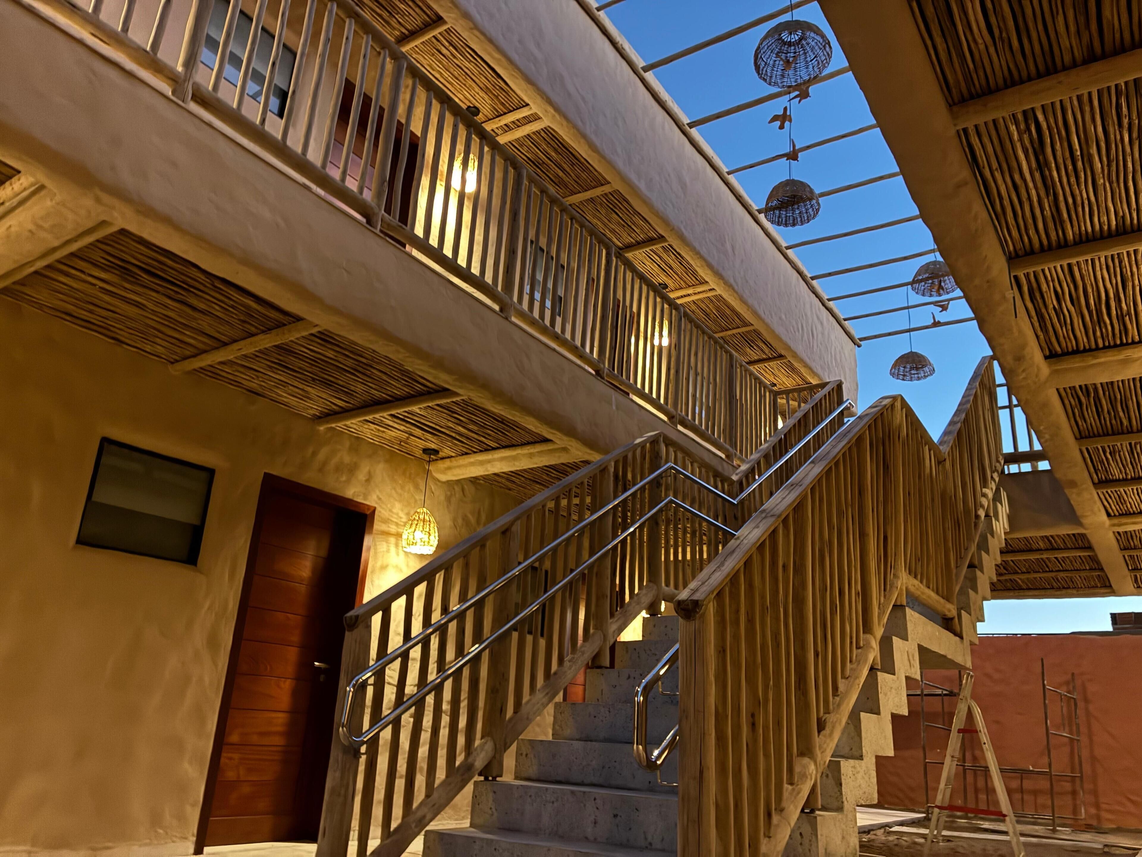Una escalera con barandillas de madera y una barandilla metálica que lleva a un nivel superior con vista al cielo.
