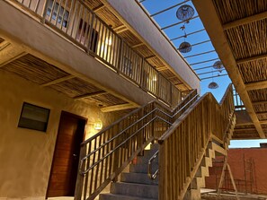 Una escalera con barandillas de madera y una barandilla metálica que lleva a un nivel superior con vista al cielo.