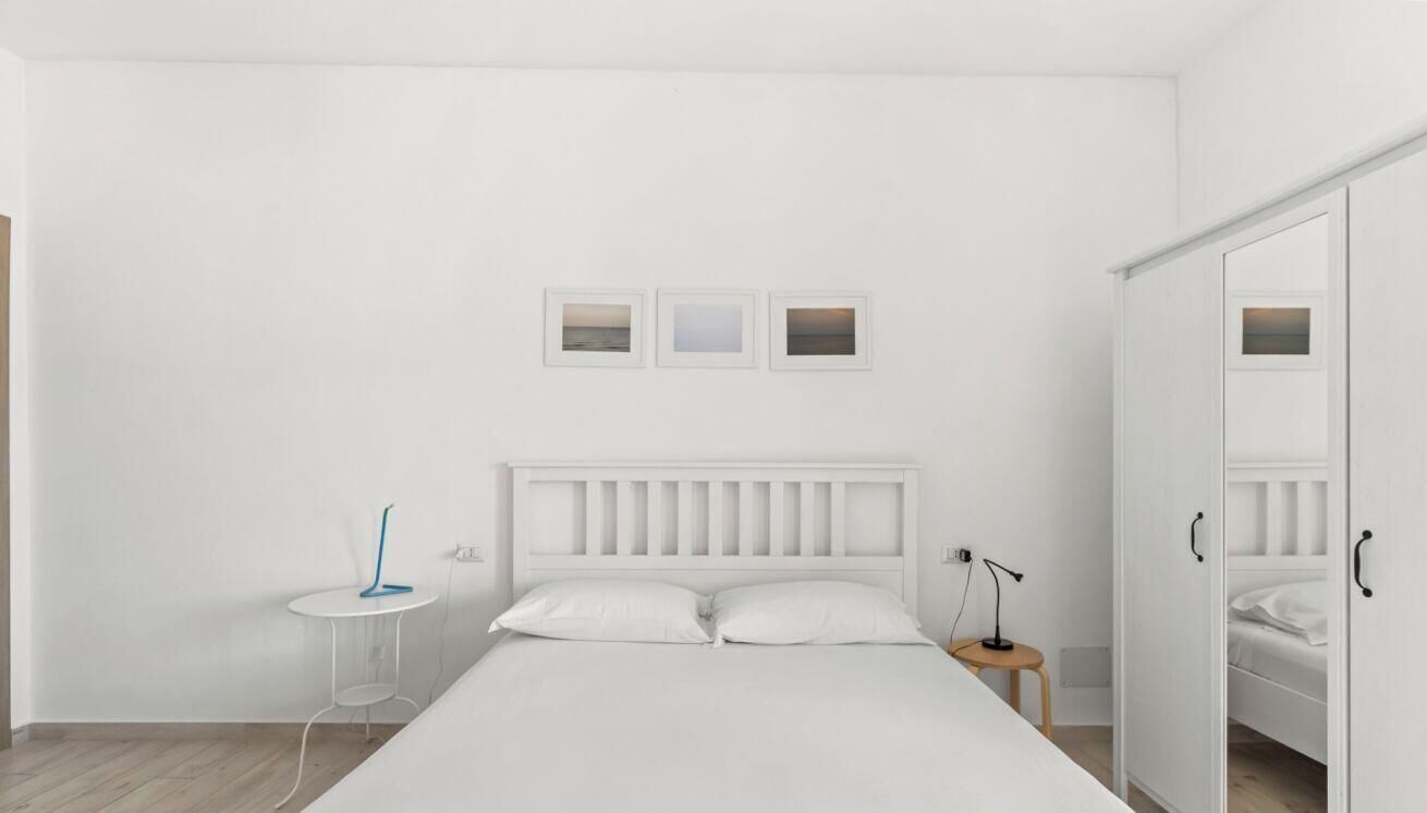 Ein schlicht eingerichtetes Schlafzimmer mit einem weißen Bett, Nachttischen und einem Kleiderschrank.