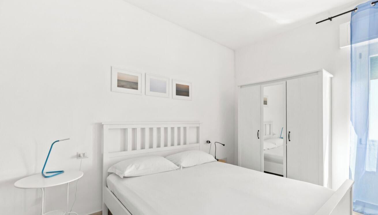 Een witte slaapkamer met een bed, nachtkastje en garderobe.