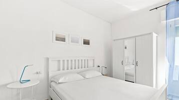 Een witte slaapkamer met een bed, nachtkastje en garderobe.