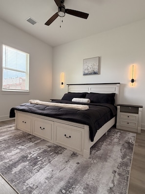 Ein Schlafzimmer mit Bett, Nachttischen, Deckenventilator, Fenster und Wandleuchten.