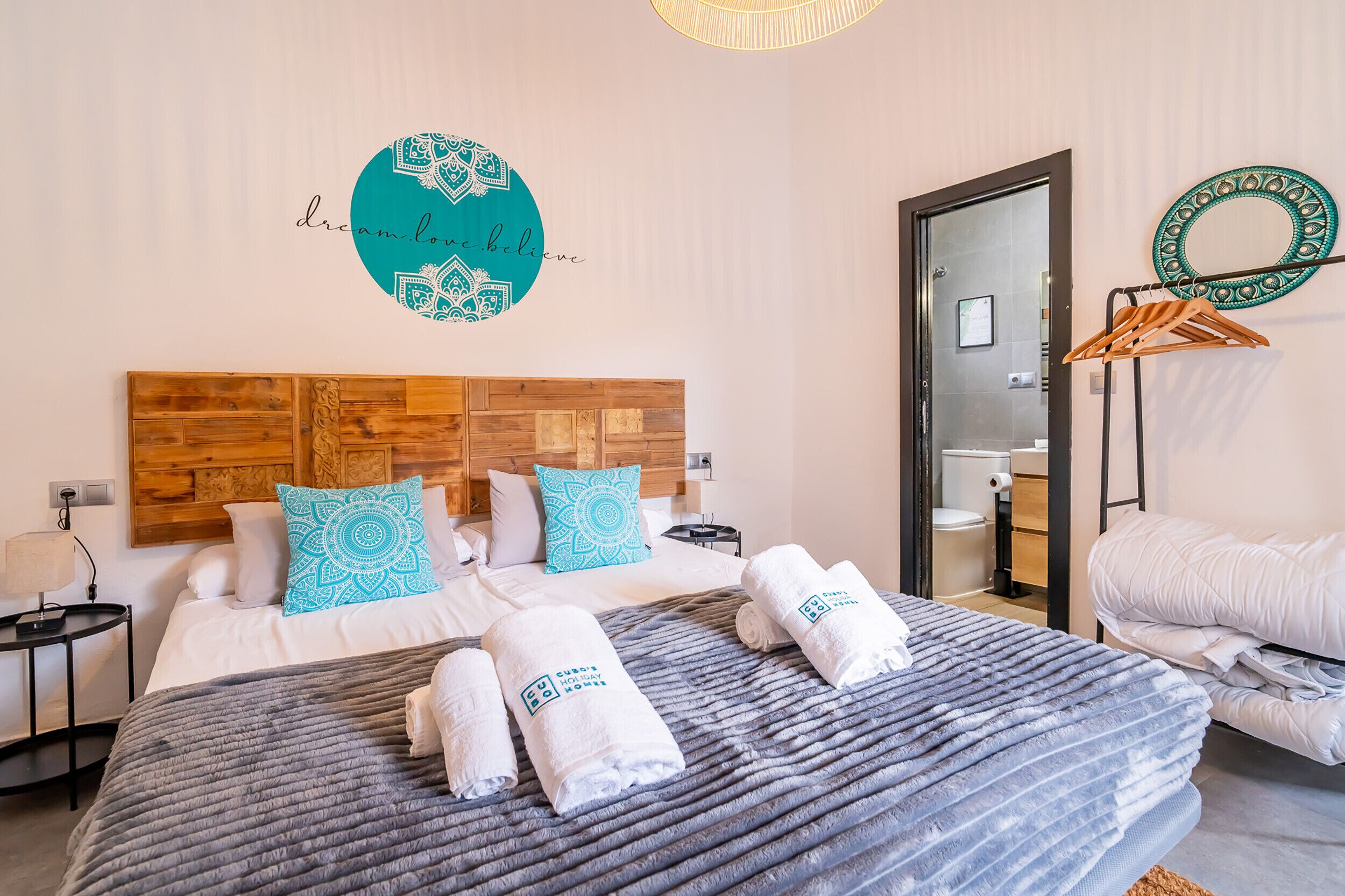Une chambre d’hôtel avec un lit, une tête de lit en bois, un mur orné d’un motif circulaire et une salle de bain visible à travers une porte ouverte.