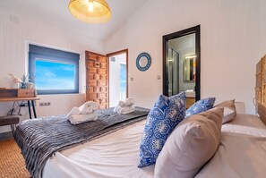 A hotel room with a bed, a desk, a window with a view, and a door leading to another room. - Cubo's Cortijo Pura Paz Retreat / Private pool / Air conditioning / BBQ / Free Wi-Fi (Casarabonela)