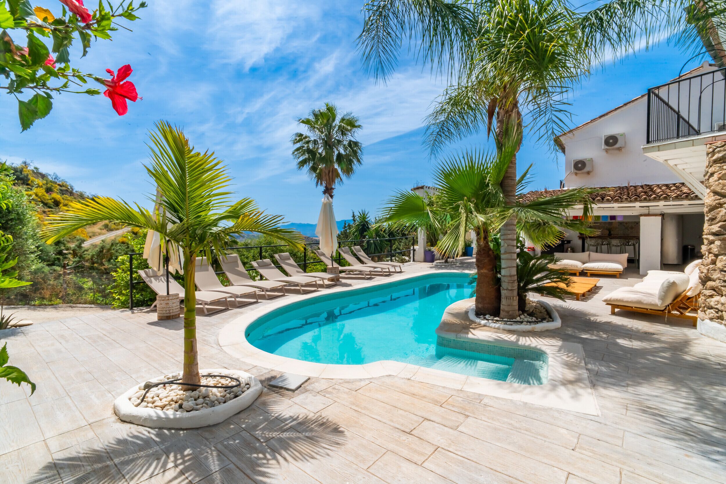 Une piscine avec des chaises longues, des palmiers et un bâtiment doté d’un balcon.