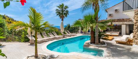 Une piscine avec des chaises longues, des palmiers et un bâtiment doté d’un balcon.