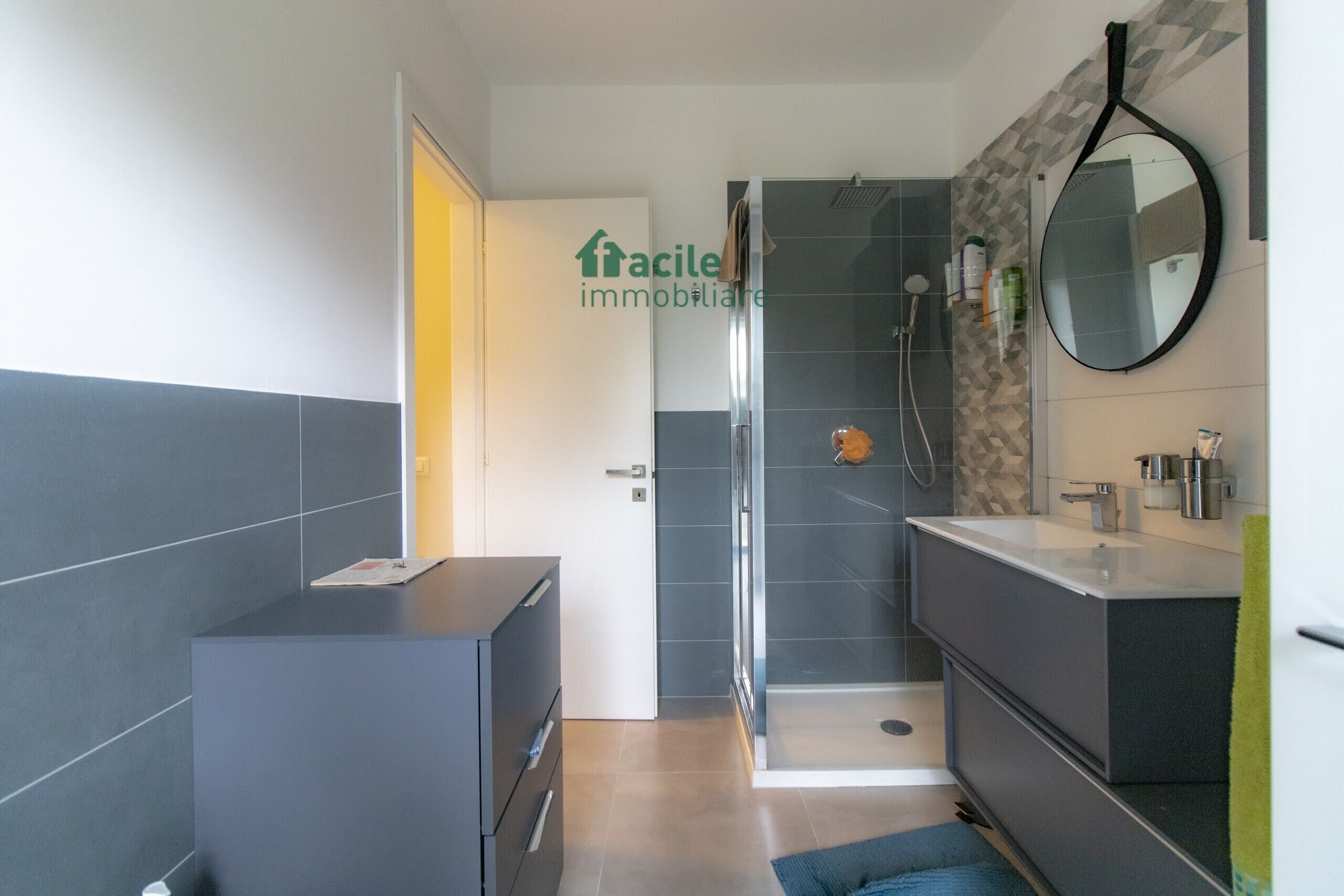Ein modernes Badezimmer mit Dusche, Waschtisch und Spiegel sowie einer Tür mit einem Schild.