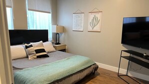 A bedroom with a bed, bedside table, lamp, wall art, TV, and wooden flooring. - #101- Spacious 2-bedroom apartment in La Grande. (La Grande)