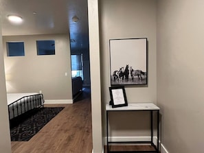 A hallway with a bed, a small table with a framed picture, and a rug.