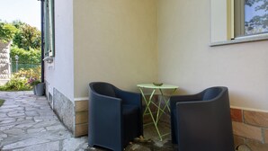 Un coin aménagé avec deux fauteuils et une petite table, un chemin pavé de pierres et la façade d’un bâtiment.