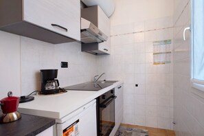 Cuina compacta amb armaris blancs, cafetera, un bany i una finestra.