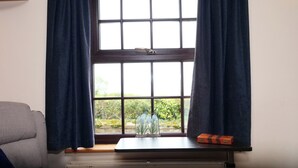 Une pièce avec une fenêtre, un radiateur, une petite table sur laquelle se trouvent un vase et une boîte, et un canapé gris.