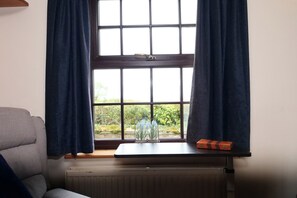 Ein Zimmer mit Fenster, Heizkörper, einem kleinen Tisch mit Vase und Schachtel sowie einem grauen Sofa.
