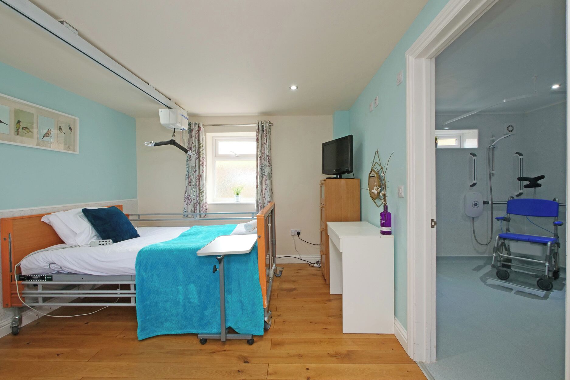 A hospital room with a bed, a desk, a television, and a shower area.