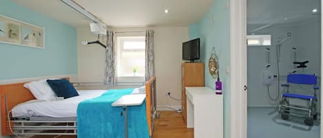 A hospital room with a bed, a desk, a television, and a shower area.