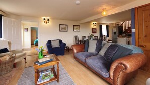 Un salon avec un canapé, un fauteuil, une table basse et, au fond, un coin repas.