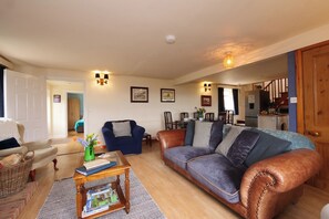 Ein Wohnzimmer mit Sofa, Sessel, Couchtisch und einem Essbereich im Hintergrund.
