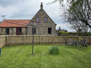 Ein Steinhaus mit rotem Ziegeldach, einem Holzzaun und einem grünen Rasen.