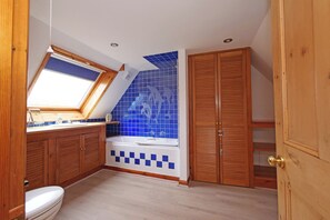 Ein Badezimmer mit Dachfenster, einer Badewanne und blauen Mosaikfliesen.