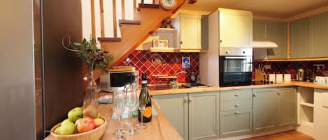 A kitchen with a wooden counter, a bowl of fruit, wine glasses, and a clock on the wall.