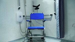 Un fauteuil d’examen médical équipé de roulettes, d’un panneau de commande et d’un système de ventilation, dans un environnement clinique.