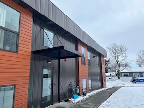 A modern building with a combination of wooden and metal siding, large windows, and a covered entrance.