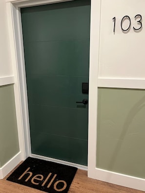 A door with a green door number '103' and a black doormat with 'hello' on it.