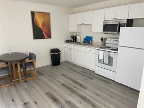 Una cocina moderna con gabinetes blancos, un microondas de acero inoxidable, un horno y un comedor con mesa y sillas.