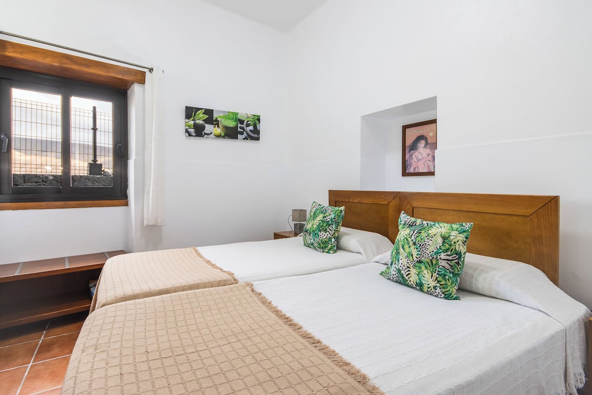 A hotel room with two beds, a window with curtains, a small table, and a wall with a picture and a framed photo.