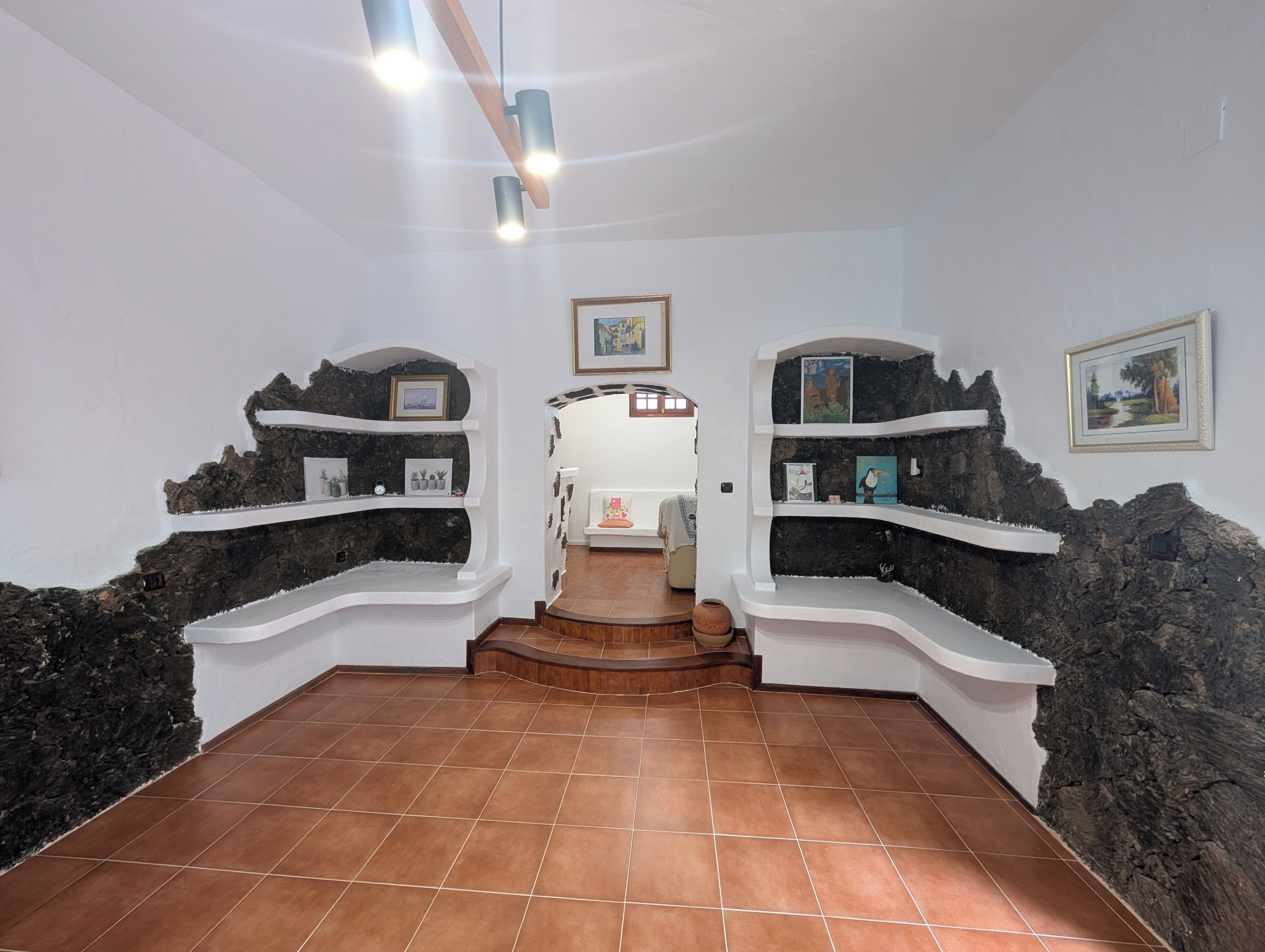 Una hall con pavimento piastrellato, pareti bianche e mensole con quadri incorniciati.