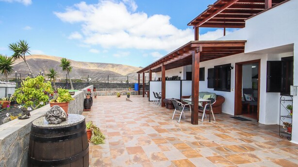 A covered patio with a view of mountains, outdoor seating, and potted plants.