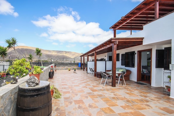 A covered patio with a view of mountains, outdoor seating, and potted plants.